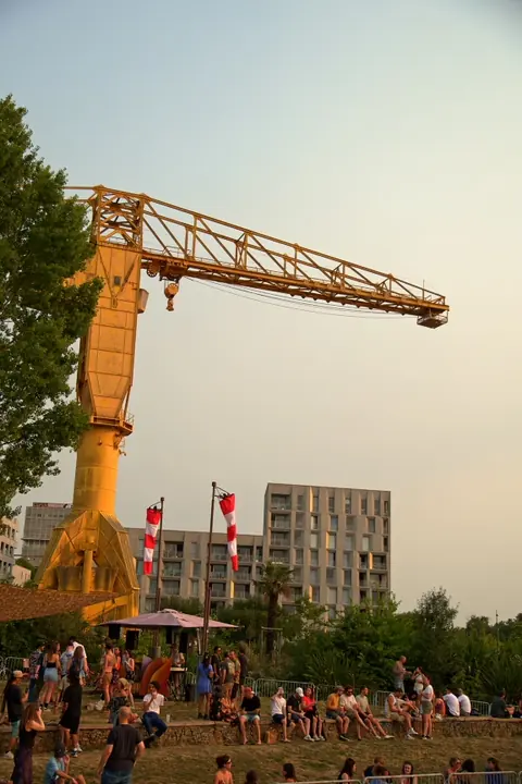 Le public installé au pied de la grue jaune de l’île de Nantes, sous des manches à air, au coucher du soleil.