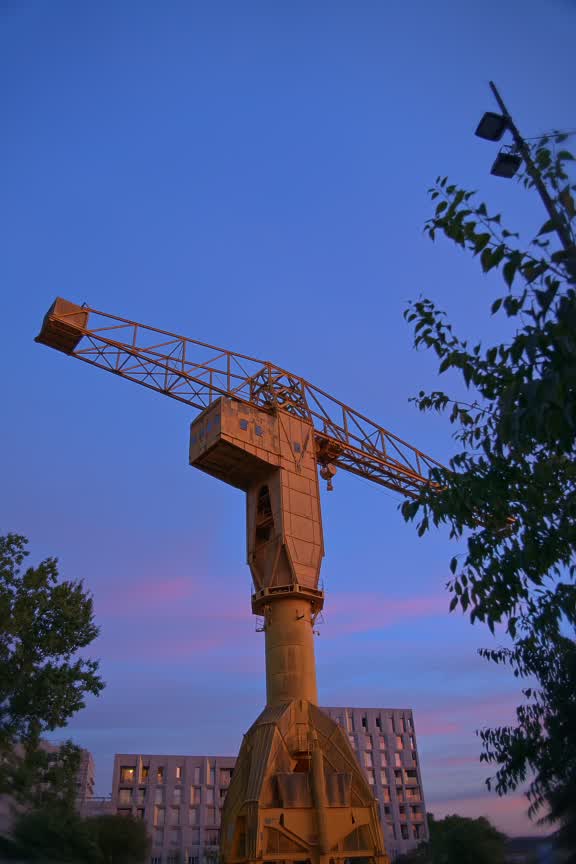 La grue jaune de l’île de Nantes se découpe sur un ciel bleu et rose au coucher du soleil.